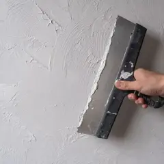 Ręka trzymająca kielnię, która rozprowadza gładzie na ścianie, tworząc artystyczną fakturę.