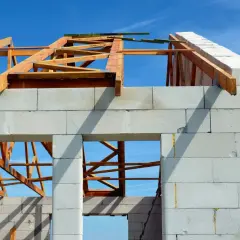 Budowa domu z bloczków silikatowych, widoczna drewniana konstrukcja dachu na tle błękitnego nieba.