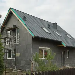 Trwa remont starego domu. Szara bryła z nowym dachem, oknami i rusztowaniami czeka na wykończenie.