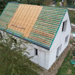 Dom w budowie, widoczne etapy budowy domu: ściany z bloczków, przygotowany dach pod pokrycie.