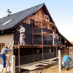 Pracownicy na rusztowaniach ocieplają dom. Określenie ceny ocieplenia za 1m2 robocizna wymaga analizy.