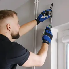 Mężczyzna w rękawicach mierzy ścianę, przygotowując się do montażu rur pp.