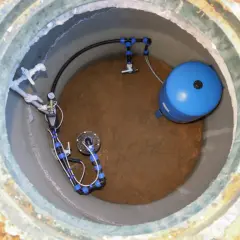 Wnętrze studni głębinowej z pompą, niebieskim zbiornikiem hydroforowym i instalacją hydrauliczną.