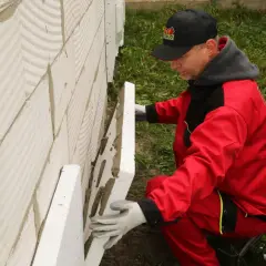Budowlaniec w czerwonym stroju montuje płyty styropianowe o odpowiedniej grubości na ścianie z bloczków.