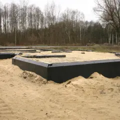 Fundamenty domu w piasku, z czarną folią zabezpieczającą przed wilgocią. To kluczowy etap budowy – izolacja pozioma fundamentów.