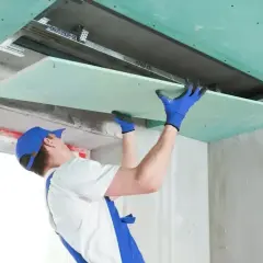 Pracownik montuje płytę gk, dopasowując jej wymiary do konstrukcji sufitu podwieszanego.