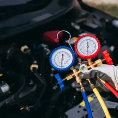 Mechanik z rękawiczką trzyma manometry do nabicia klimatyzacji. Sprawdza cenę usługi.