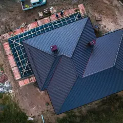 Trwa wymiana dachu na domu jednorodzinnym. Nowe pokrycie z ciemnej dachówki, widoczne kominy i rusztowania.