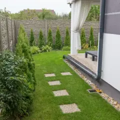 System odprowadzenia wody z rynien na trawnik, z kamiennym chodnikiem i zielonym ogrodem.