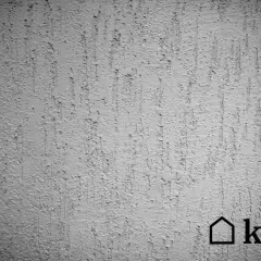 Szara ściana z fakturą tynku kornik, imitującą ślady po żerowaniu owadów. Widoczny znak wodny kb.pl.