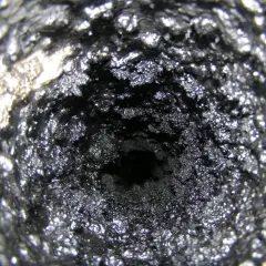 Wnętrze komina pokryte grubą warstwą sadzy i kreozotu, tworzącą chropowatą, ciemną powierzchnię.