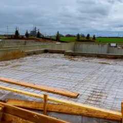 Budowa domu w toku. Betonowe ławy fundamentowe otaczają plac budowy, na którym rozłożono siatkę zbrojeniową.