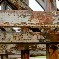 Metalowe belki konstrukcji pokryte rdzą i łuszczącą się farbą. To przykład tego, co to jest korozja, niszcząca metal.