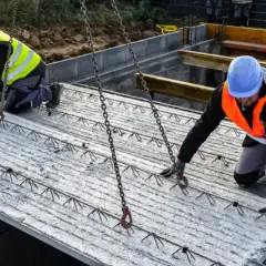 Dwóch budowlańców w kamizelkach odblaskowych przygotowuje strop filigran do montażu.
