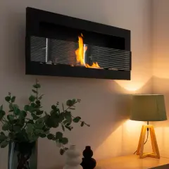 Płomienie tańczą w nowoczesnym biokominku, który z pewnością grzeje. Obok bukiet eukaliptusa i lampka tworzą przytulną atmosferę.