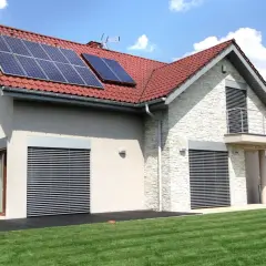 Nowoczesny dom z panelami solarnymi na dachu, otoczony zielonym ogrodem.