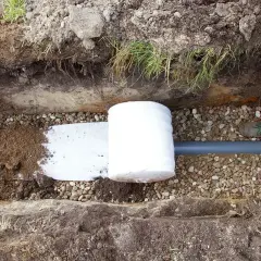 Budowa odwodnienia domu: rura drenarska owinięta geowłókniną, zasypana żwirem i ziemią.