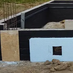 Fundamenty domu w budowie. Czarny mur z izolacją, płyta OSB i styropian. Praca murarza w toku.