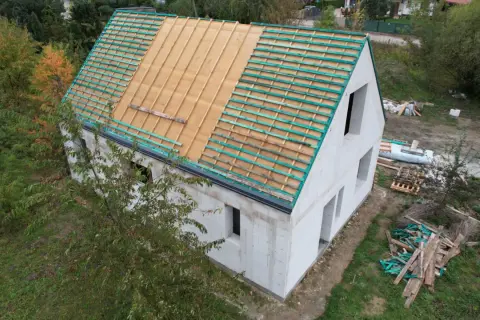 Dom w budowie, widoczne etapy budowy domu: ściany z bloczków, przygotowany dach pod pokrycie.