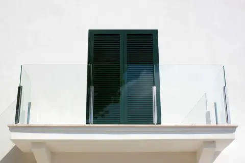 Nowoczesny balkon z przeszkloną balustradą. Okapnik nad oknem zapewnia ochronę przed deszczem.