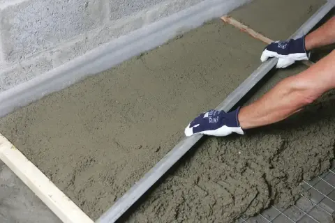 Ręce w rękawiczkach wyrównują świeży styrobeton za pomocą łaty.