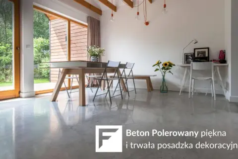 Nowoczesne wnętrze z dużymi oknami i betonem polerowanym na podłodze. W centralnej części stół jadalniany, obok biurko.