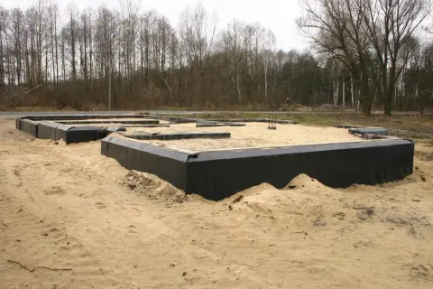 Fundamenty domu w piasku, z czarną folią zabezpieczającą przed wilgocią. To kluczowy etap budowy – izolacja pozioma fundamentów.