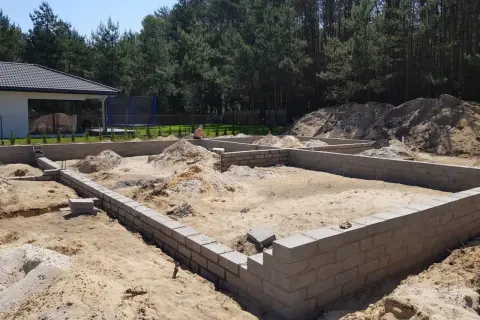 Fundamenty domu w budowie. Piasek, bloczki betonowe i kopce ziemi. To pierwszy krok, od czego zacząć budowę domu.