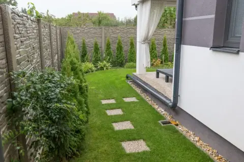System odprowadzenia wody z rynien na trawnik, z kamiennym chodnikiem i zielonym ogrodem.