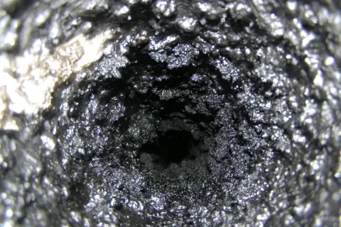 Wnętrze komina pokryte grubą warstwą sadzy i kreozotu, tworzącą chropowatą, ciemną powierzchnię.