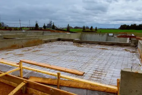 Budowa domu w toku. Betonowe ławy fundamentowe otaczają plac budowy, na którym rozłożono siatkę zbrojeniową.
