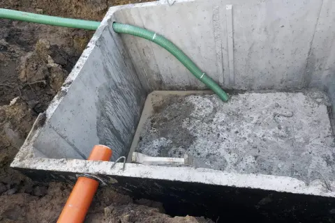 Betonowe szambo 10m3 z montażem, widoczne w wykopie z podłączonymi rurami.