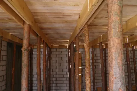 Szalowanie stropu z drewnianych belek i pni drzewnych, podtrzymujące konstrukcję nad betonowymi ścianami.