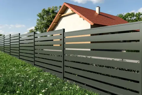Nowoczesne ogrodzenie panelowe w ciemnoszarym kolorze, z drewnianymi wstawkami, otacza dom z czerwonym dachem. Idealne rozwiązanie, by poznać koszt ogrodzenia panelowego.