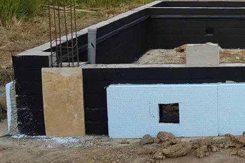 Fundamenty domu w budowie. Czarny mur z izolacją, płyta OSB i styropian. Praca murarza w toku.