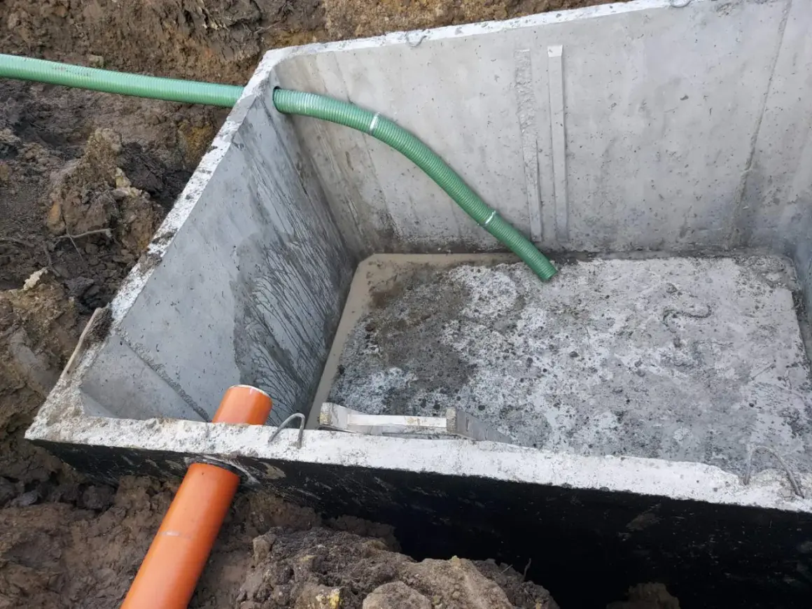 Betonowe szambo 10m3 z montażem, widoczne w wykopie z podłączonymi rurami.