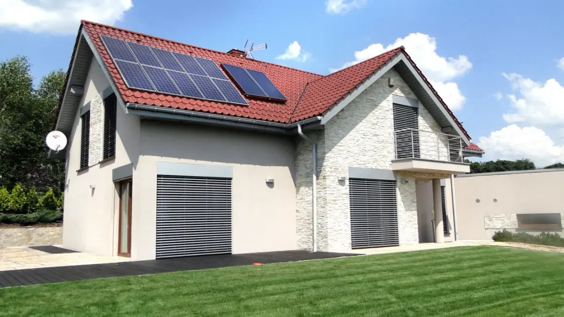 Nowoczesny dom z panelami solarnymi na dachu, otoczony zielonym ogrodem.