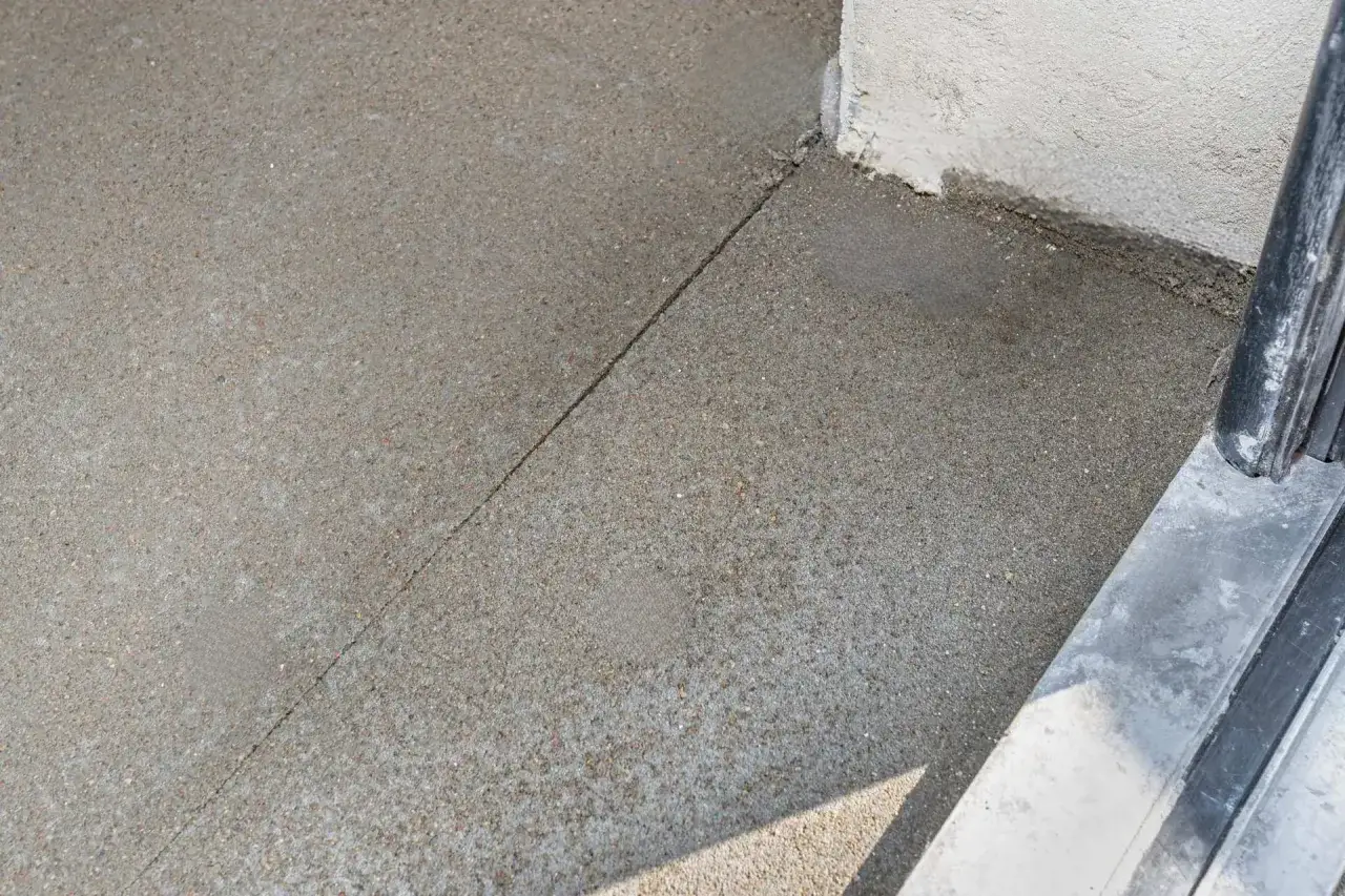 Szara powierzchnia betonu z widoczną linią dylatacji biegnącą od rogu budynku.