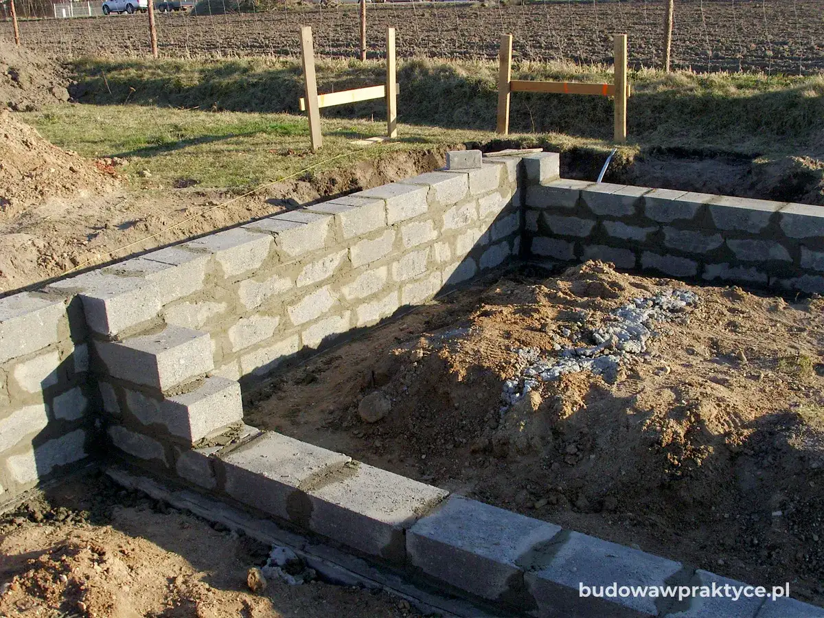 Fundament z bloczków betonowych, widać różne wymiary cegły i postęp prac budowlanych.