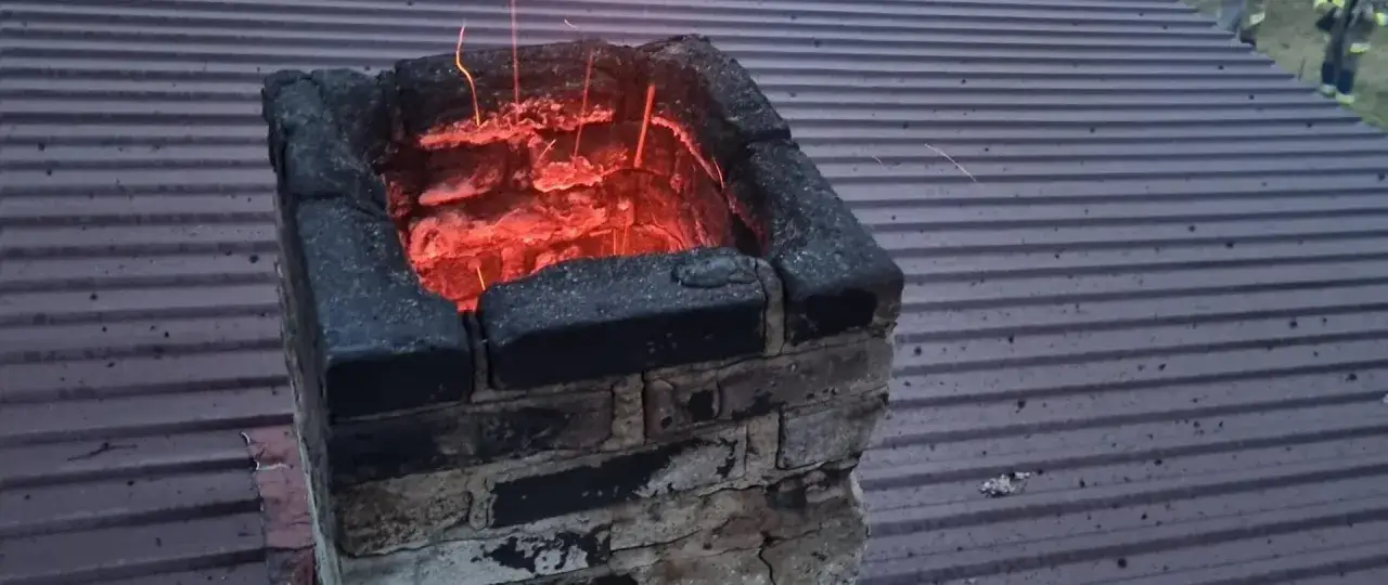 Żarzący się komin, w którym gromadzi się niebezpieczny kreozot, grozi pożarem. Iskry unoszą się nad dachem.