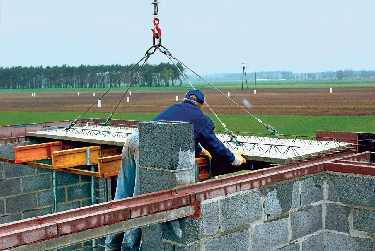 Robotnik z pomocą dźwigu montuje strop filigran na budowie.