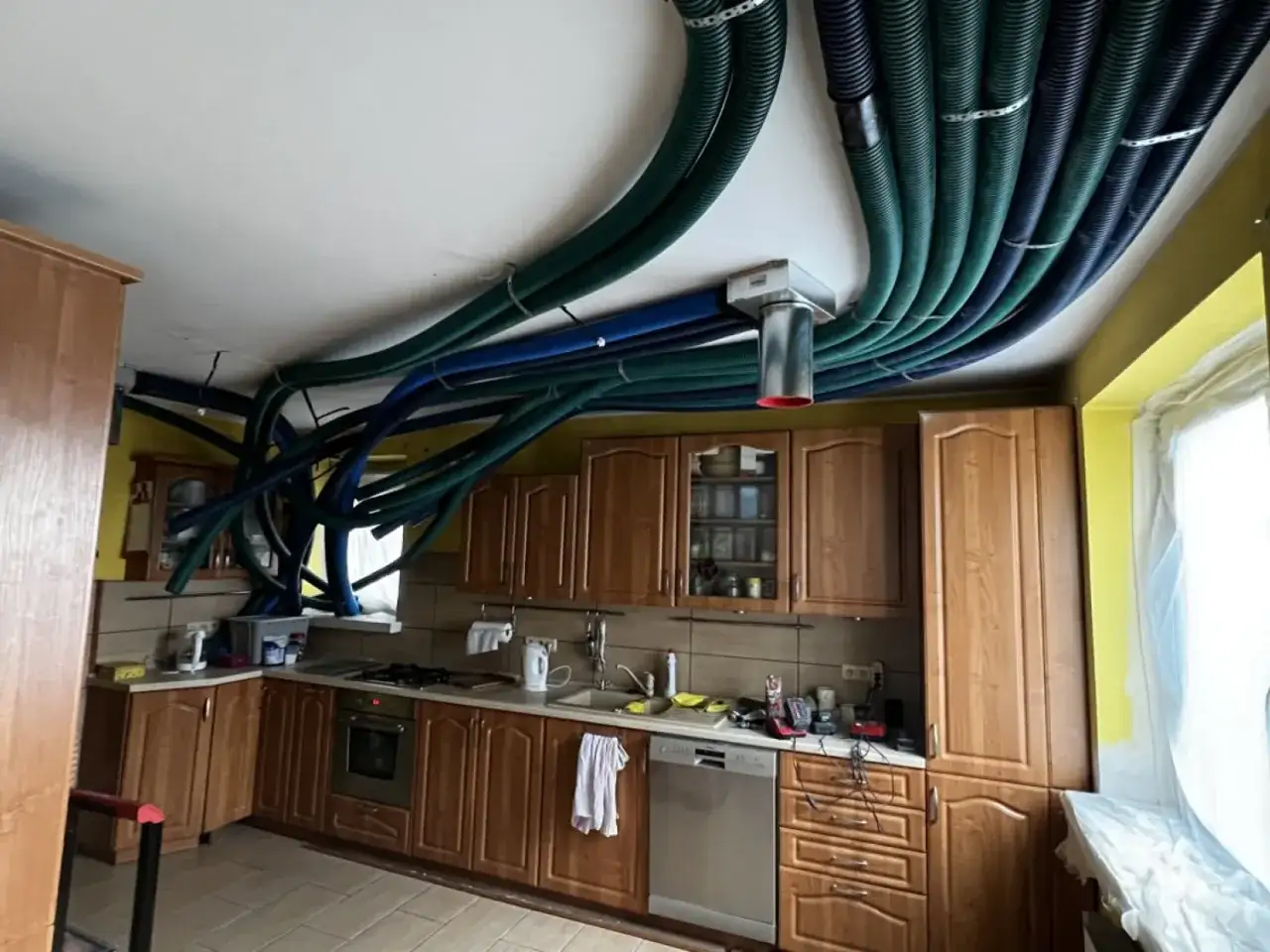 Instalacja rekuperacji w starym domu. W kuchni widoczne liczne, kolorowe przewody wentylacyjne prowadzące do centrali.