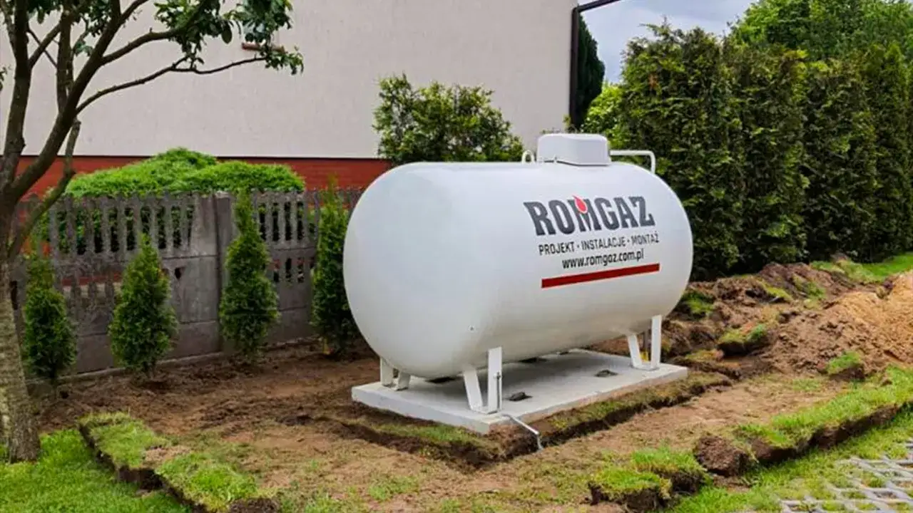 Biały zbiornik na gaz ziemny, gotowy do instalacji ogrzewania gazowego. Obok teren przygotowany do prac.