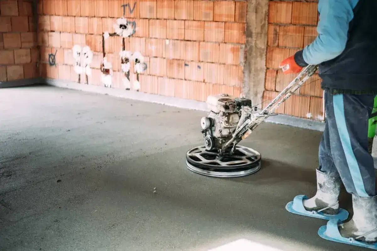 Pracownik wykonuje zacieranie betonu za pomocą mechanicznej zacieraczki.