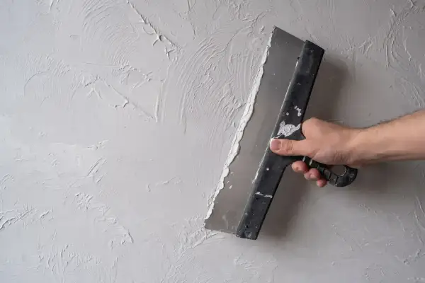 Ręka trzymająca kielnię, która rozprowadza gładzie na ścianie, tworząc artystyczną fakturę.
