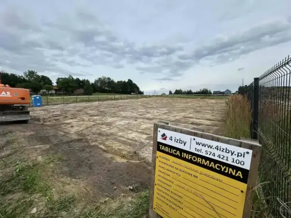 Tablica informacyjna budowy na placu budowy z koparką i toaletą.