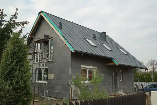 Trwa remont starego domu. Szara bryła z nowym dachem, oknami i rusztowaniami czeka na wykończenie.