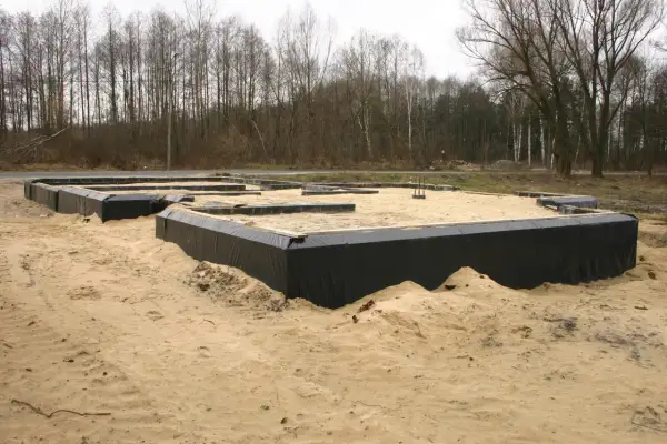 Fundamenty domu w piasku, otoczone czarną folią. W tle las. Wkrótce powstanie tu chudy beton.
