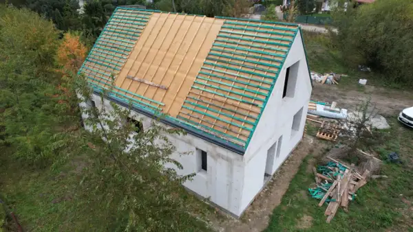 Dom w budowie, widoczne etapy budowy domu: ściany z bloczków, przygotowany dach pod pokrycie.