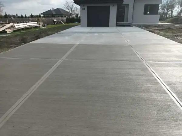 Nowy podjazd z beton stemplowany, z wyraźnymi liniami podziału, prowadzi do nowoczesnego domu.